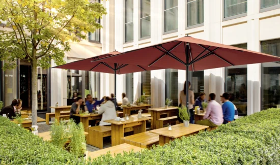 Außenbereich eines Cafés mit Holzbänken und rotem Sonnenschirm
