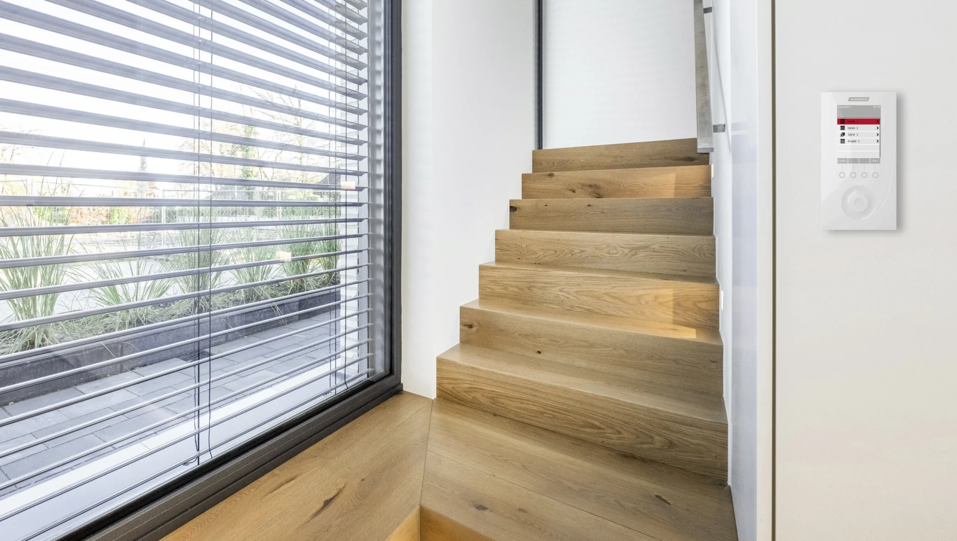 Innenansicht eines Raumes mit geöffneten Jalousien und einer Steuerungseinheit an der Wand